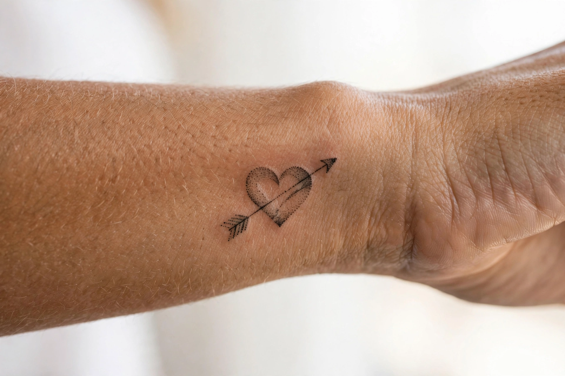 Minimal heart and arrow first tattoo for women on the forearm