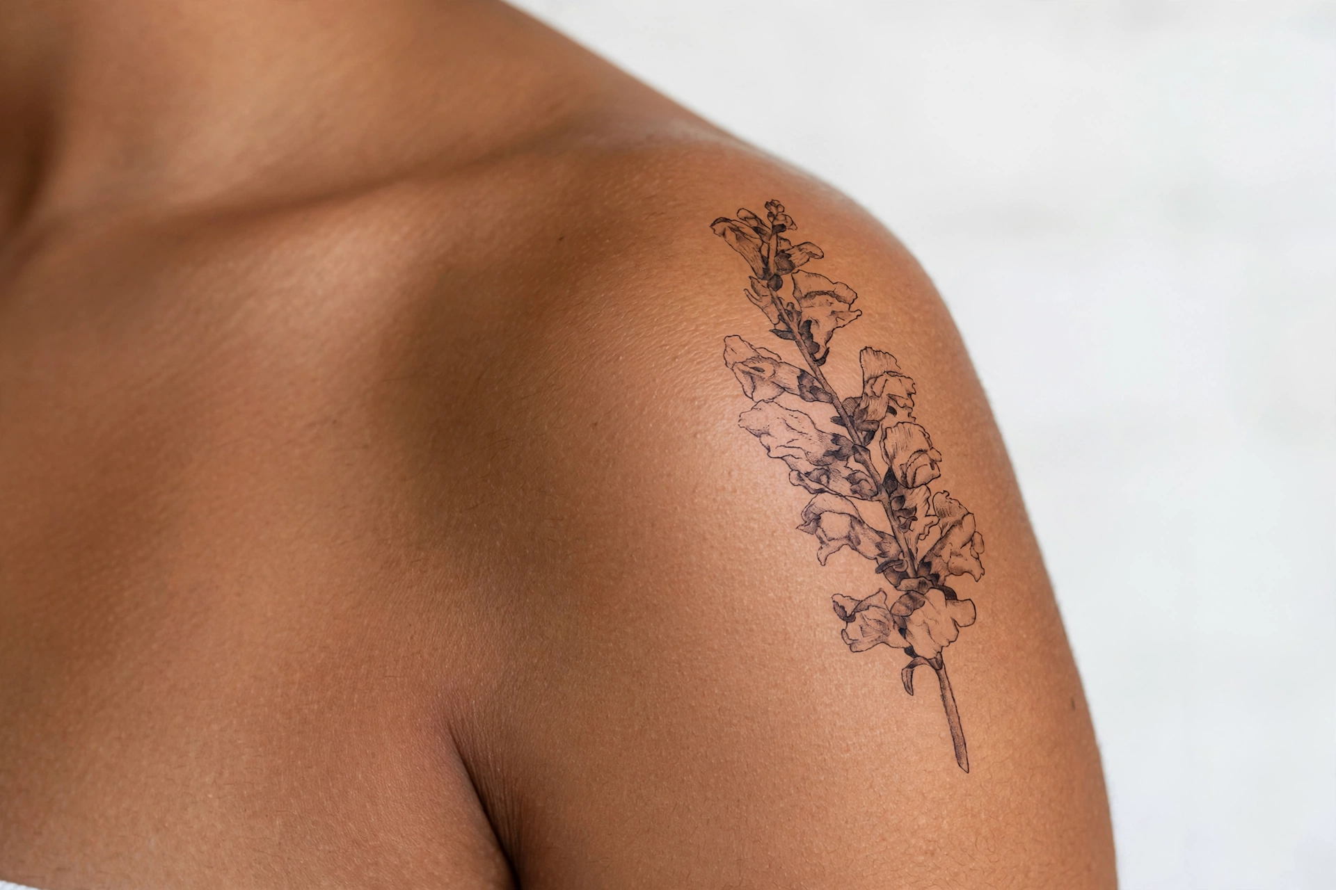 Colorful snapdragon flowers in a vertical row tattoo on a spine