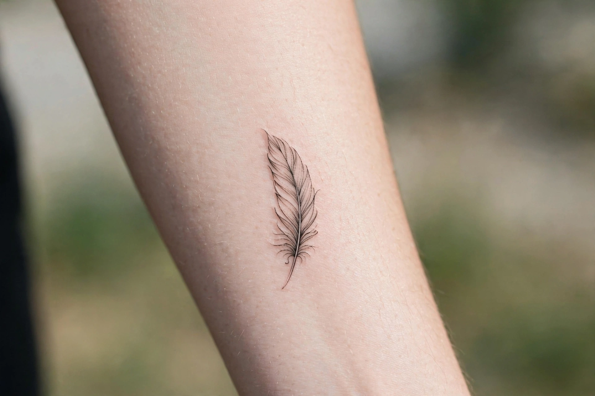 Delicate single feather memorial tattoo on the shoulder