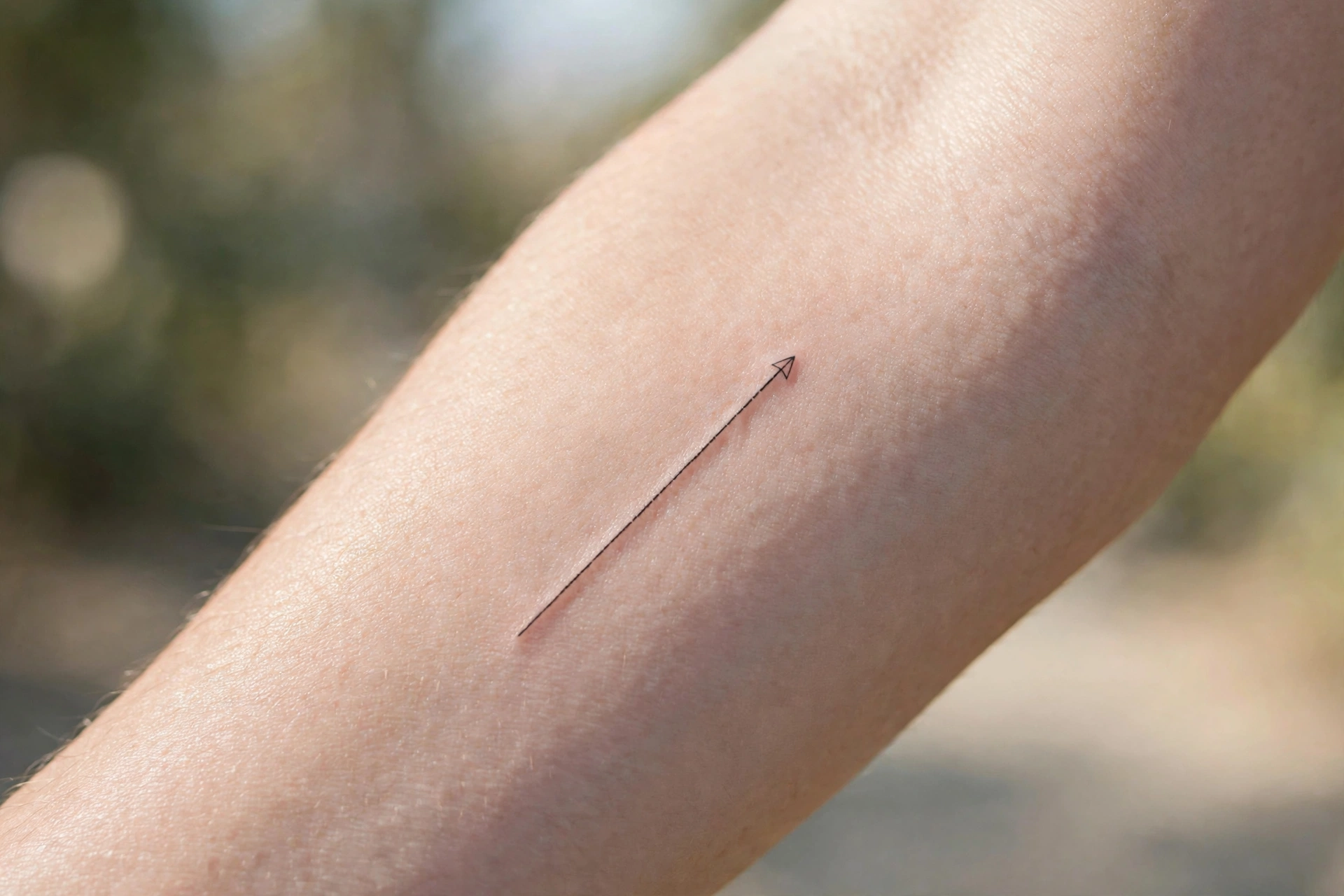 Thin arrow line minimalist tattoo on man's forearm