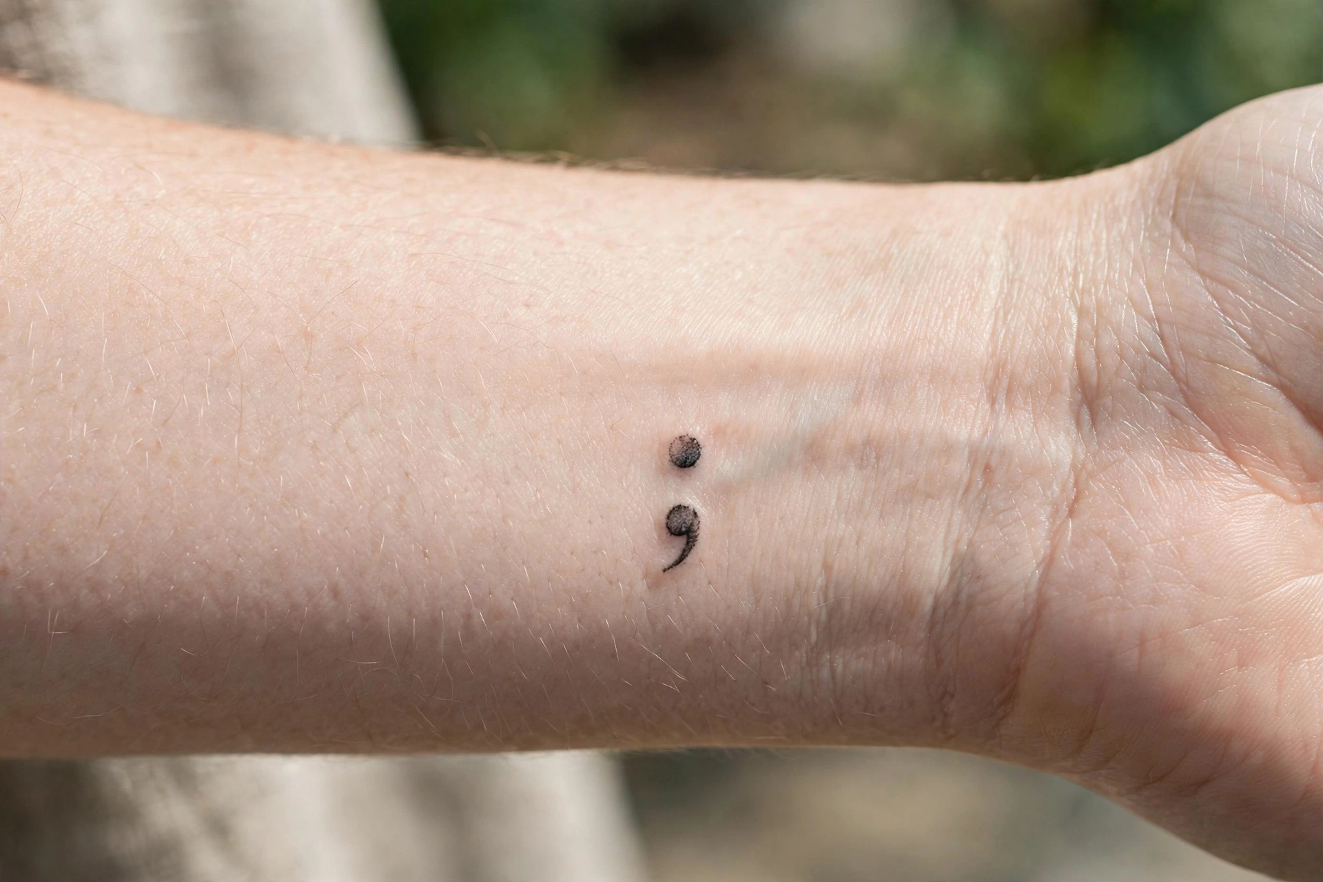 Small semicolon tattoo on man's wrist