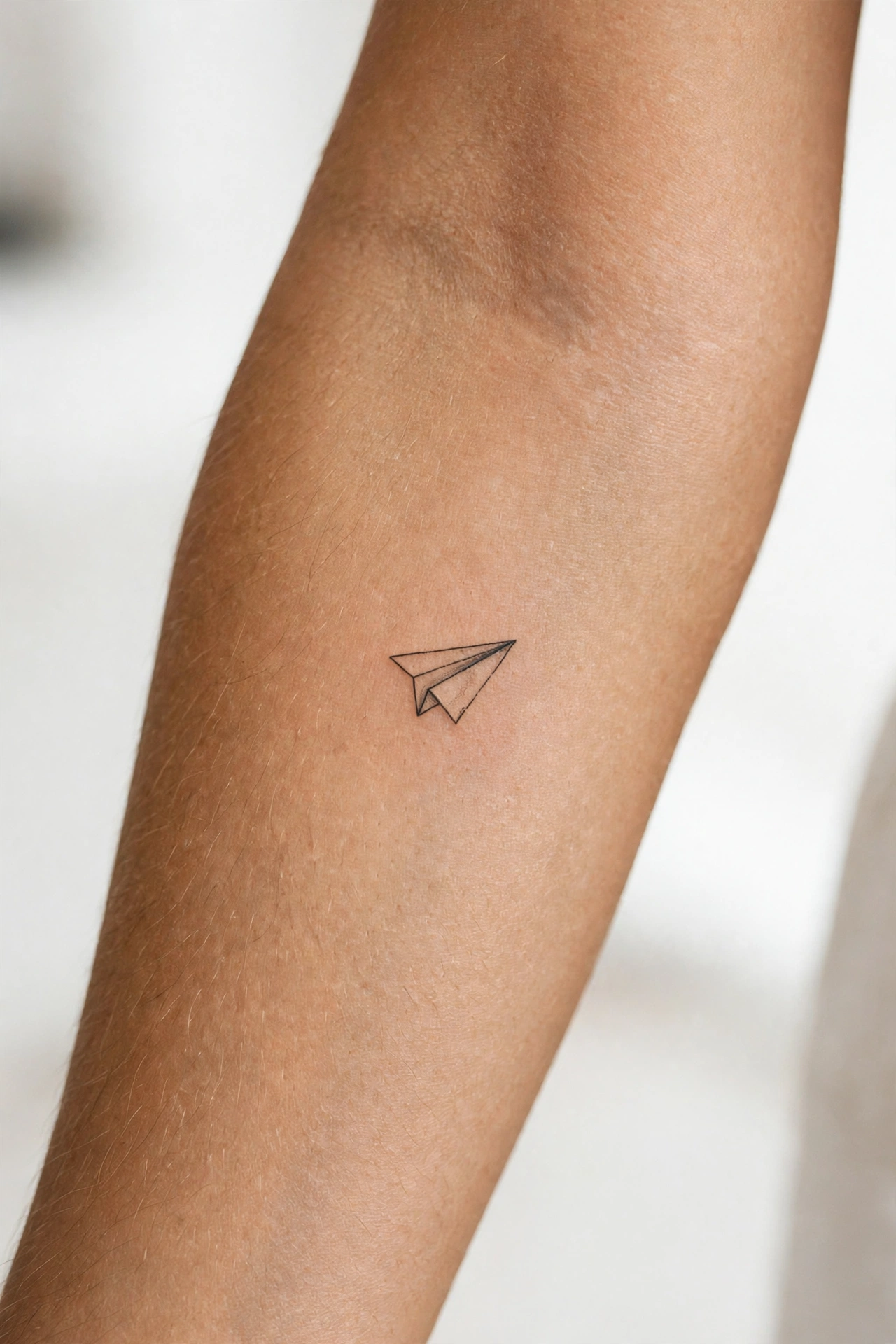 Mini paper plane tattoo on man's collarbone