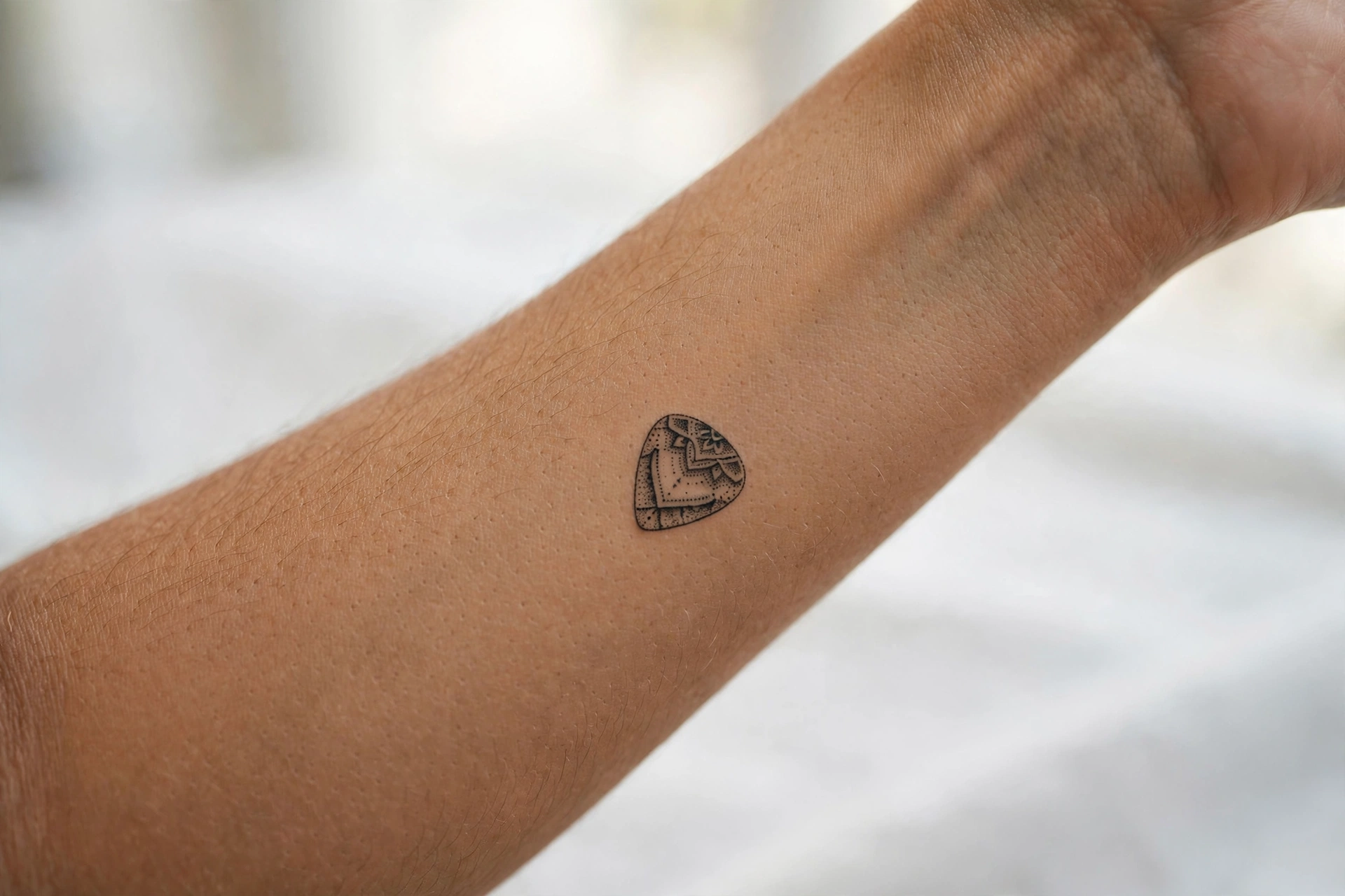 Tiny guitar pick tattoo on man's bicep