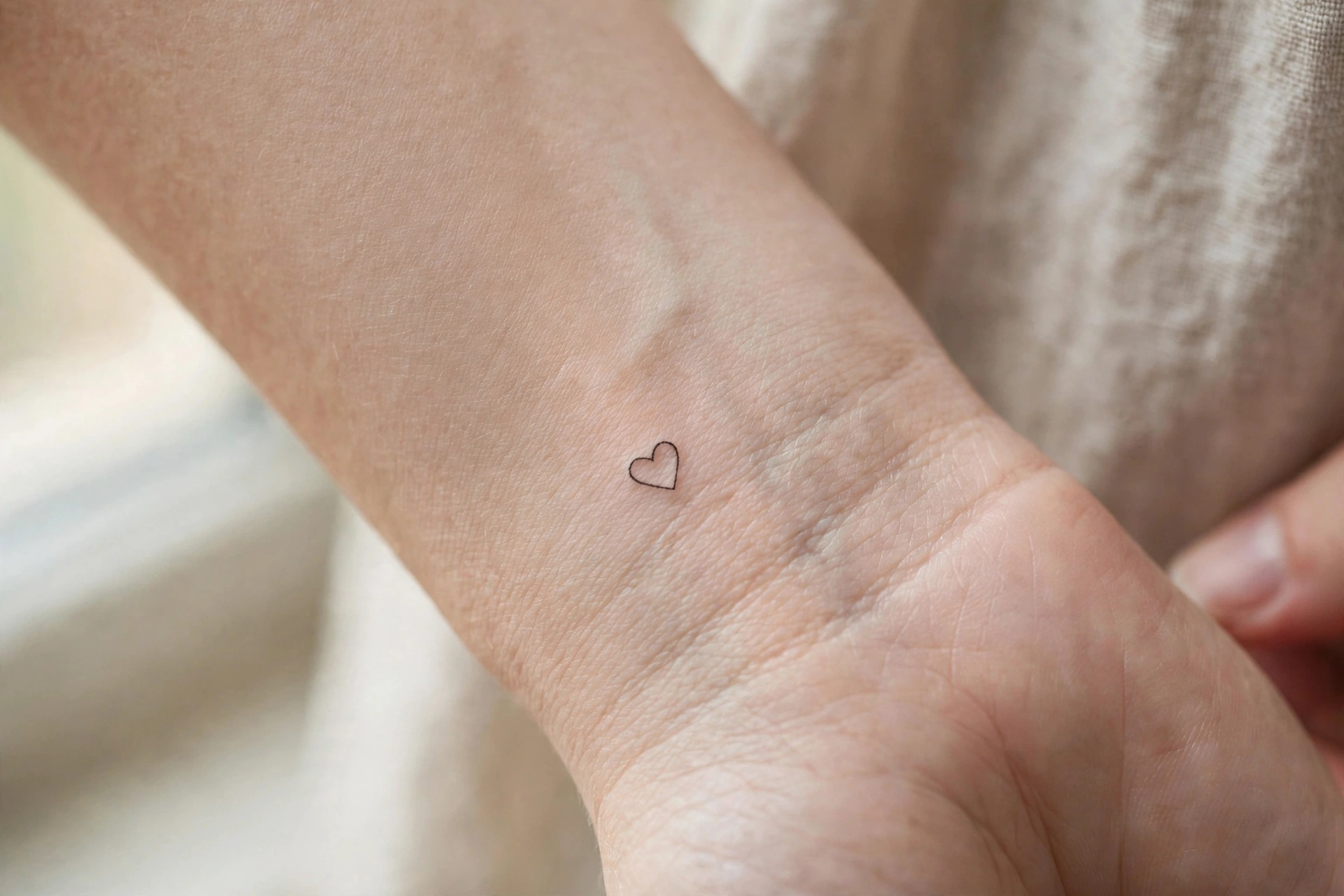 Micro outline heart tattoo smaller than a fingernail on the wrist