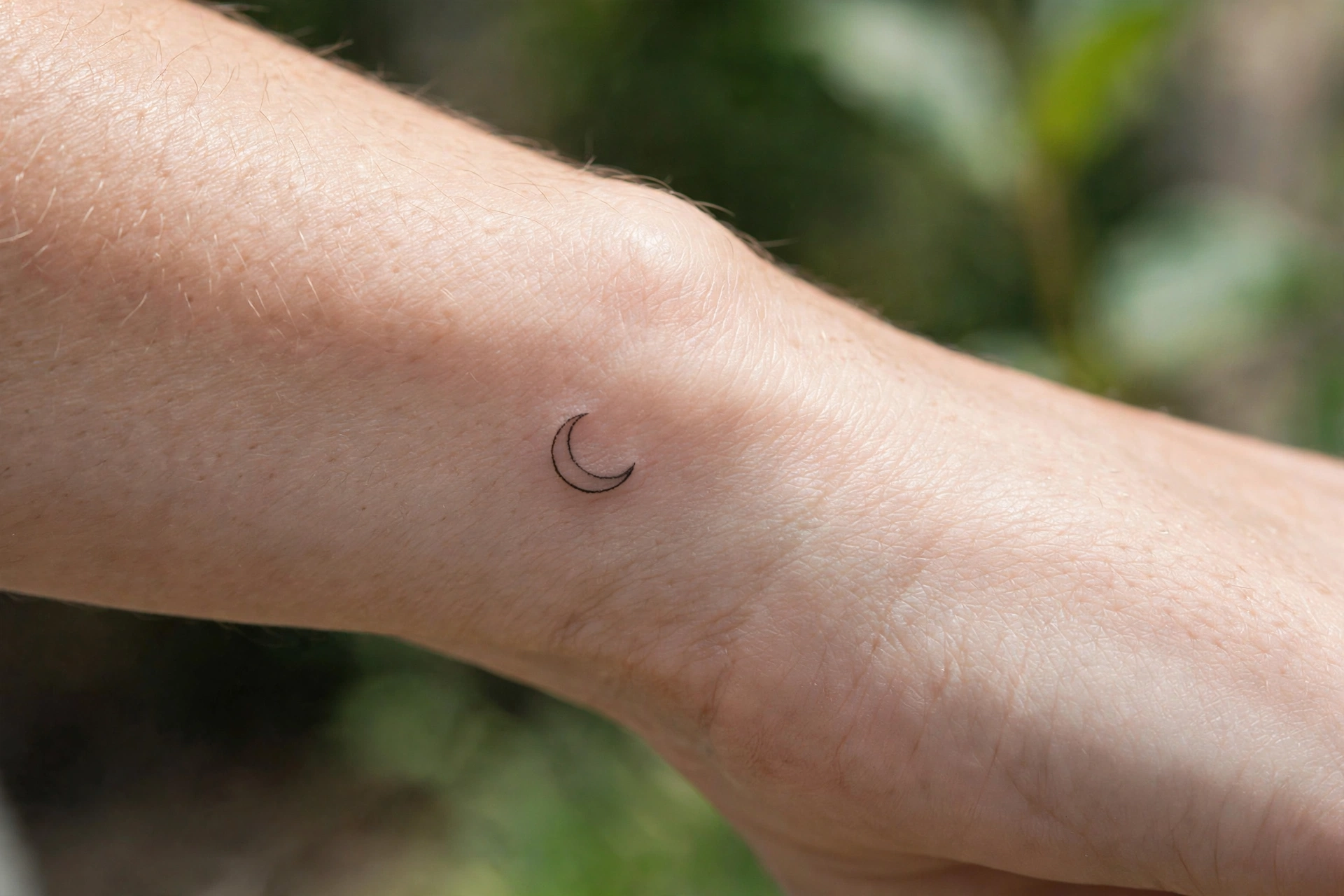 Tiny crescent moon tattoo curving along the outer wrist